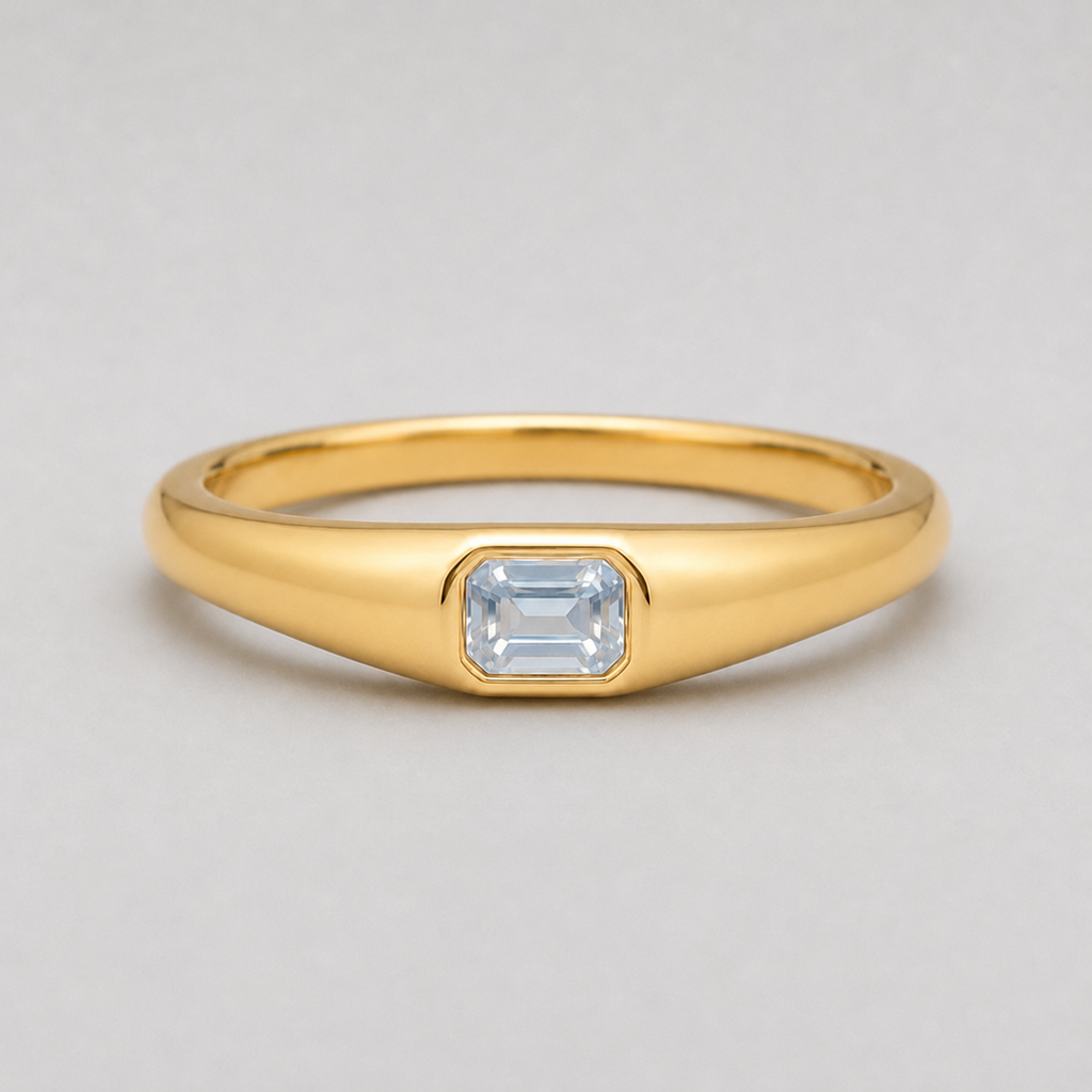 3D render of a polished yellow gold ring featuring a rectangular emerald-cut white sapphire in a bezel setting, shown on a neutral light grey background.