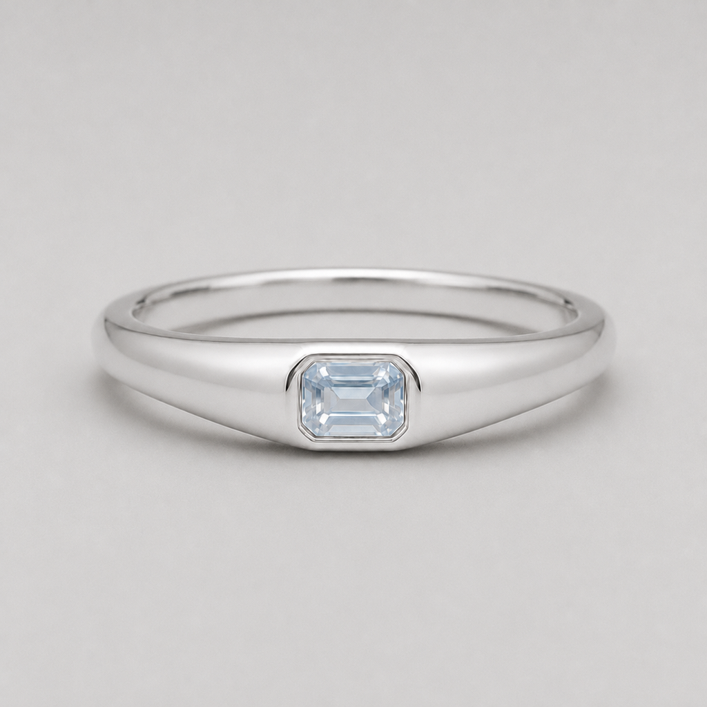 3D render of a polished silver ring featuring a rectangular emerald-cut white sapphire in a bezel setting, shown on a neutral light grey background.
