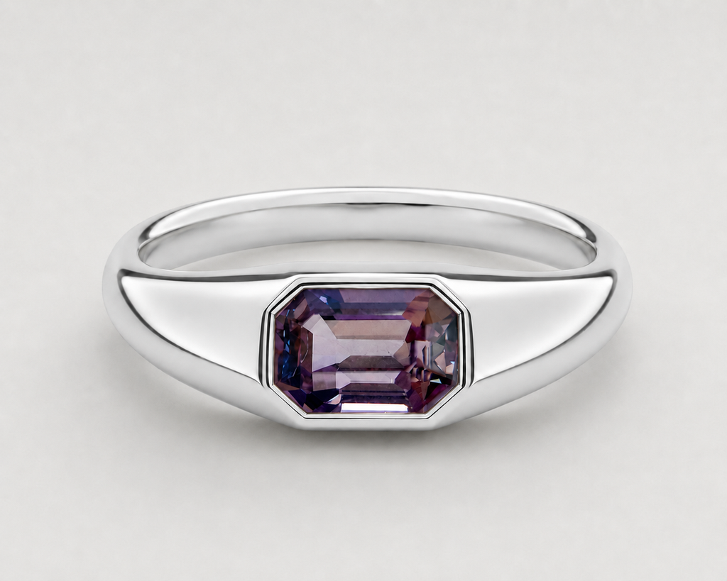 A yellow silver signet ring featuring a bezel-set emerald-cut purple spinel, shown on a neutral light grey background.