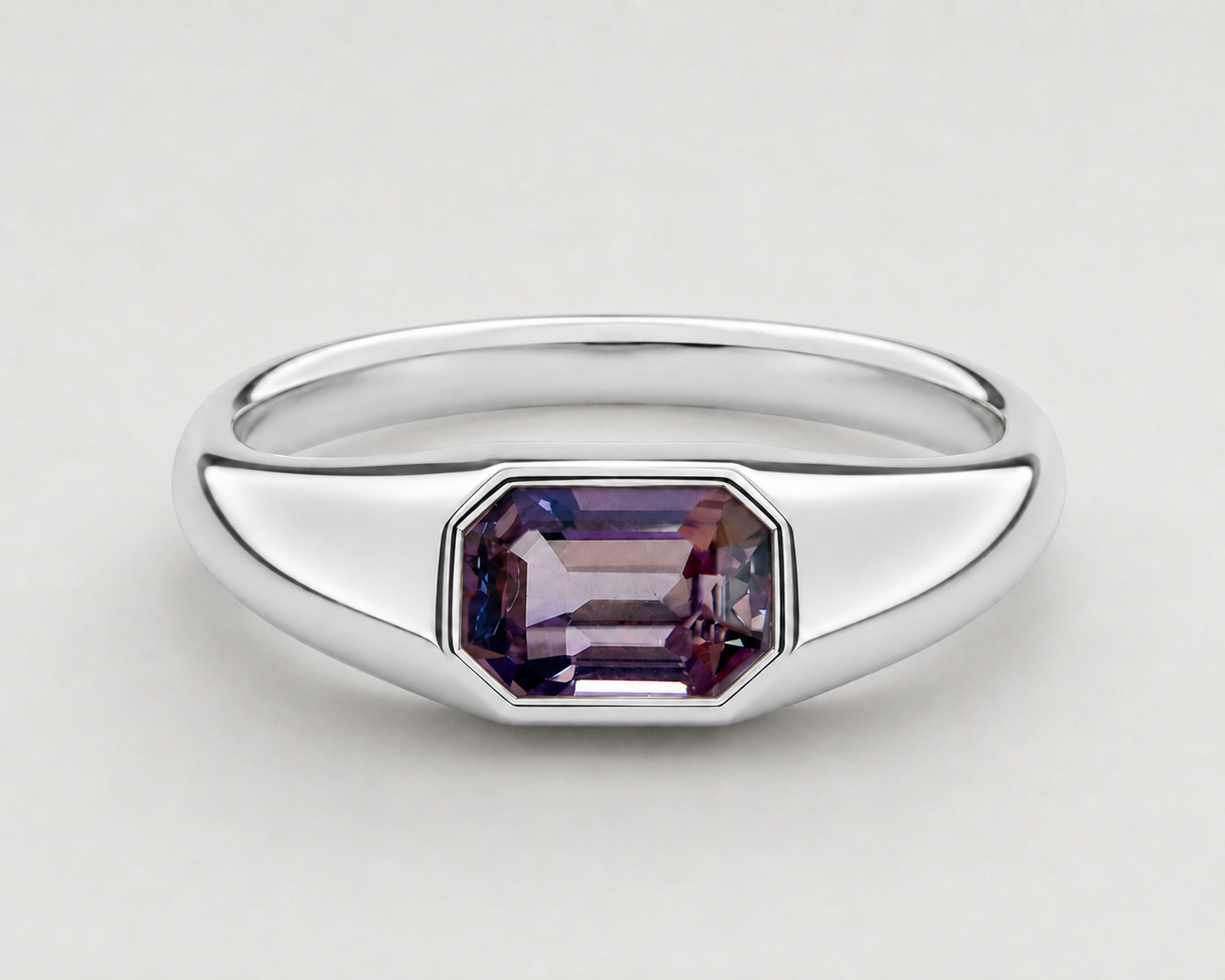 A yellow silver signet ring featuring a bezel-set emerald-cut purple spinel, shown on a neutral light grey background.