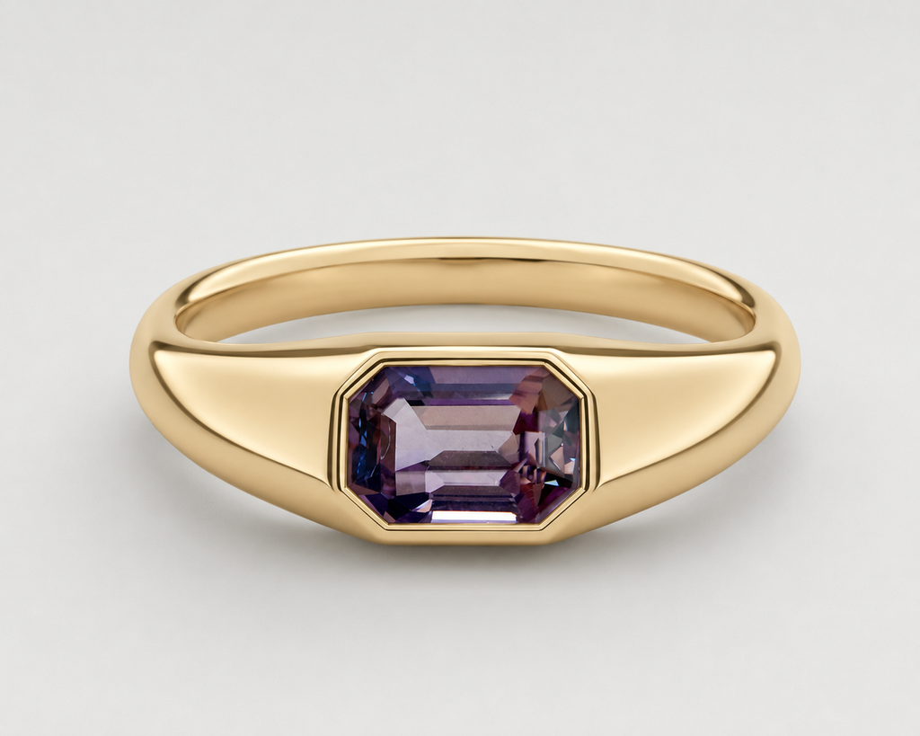 A yellow gold signet ring featuring a bezel-set emerald-cut purple spinel, shown on a neutral light grey background.