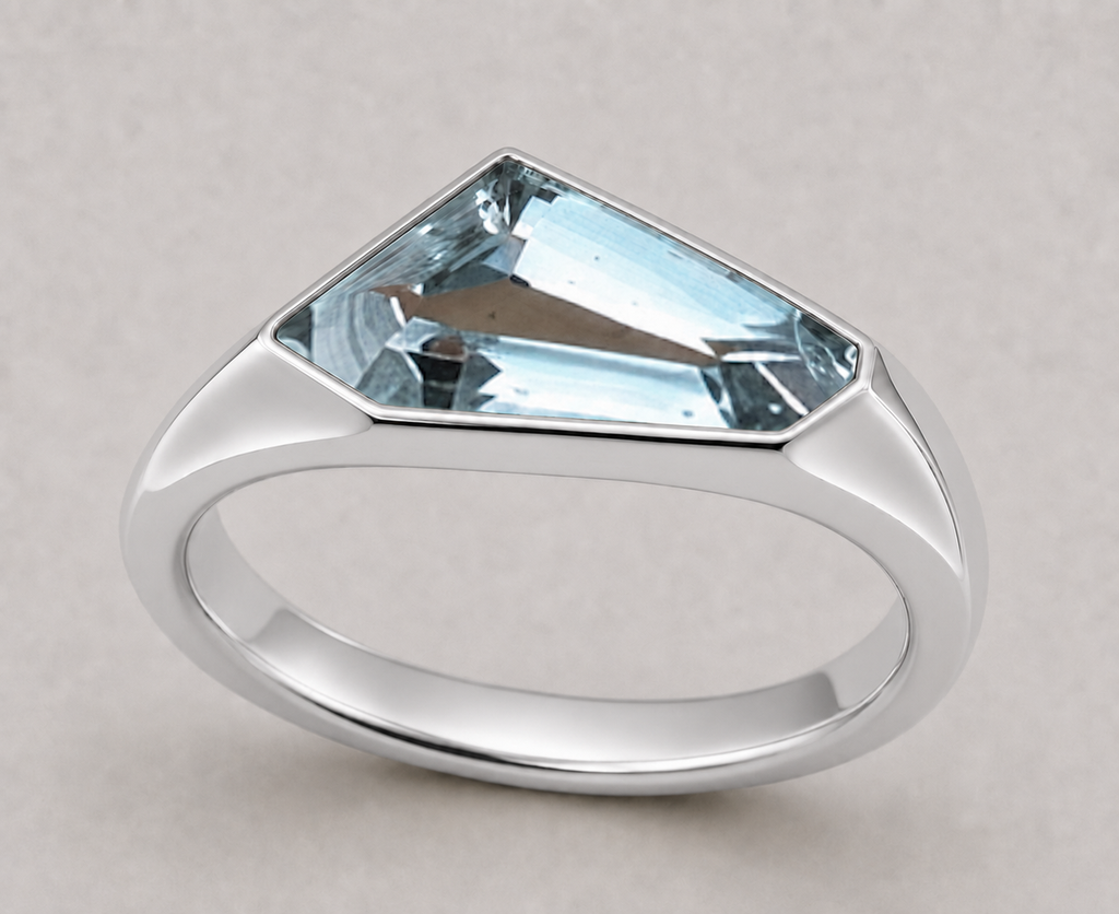 A silver signet style ring featuring a freeform aquamarine in a polished sterling silver setting, shown on a neutral light grey background.