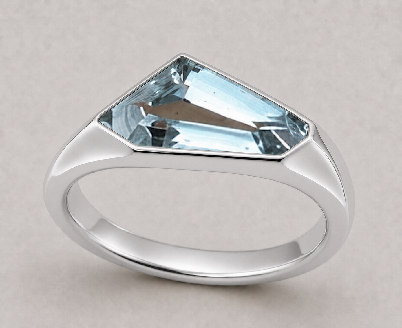 A silver signet style ring featuring a freeform aquamarine in a polished sterling silver setting, shown on a neutral light grey background.