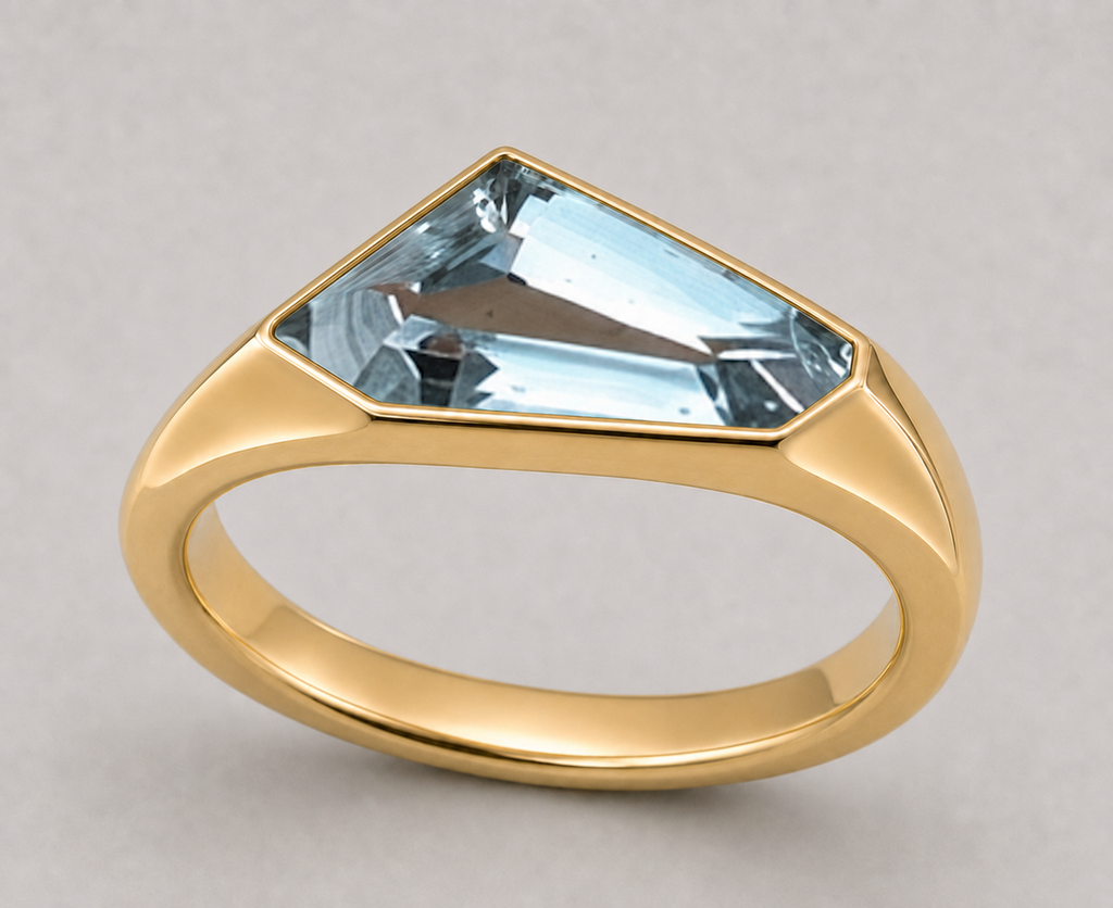 A gold signet style ring featuring a freeform aquamarine in a polished yellow gold setting, shown on a neutral light grey background.