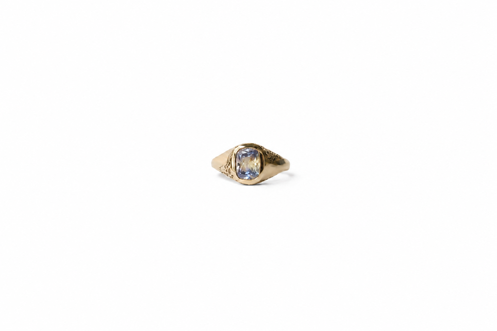 A yellow gold signet ring with a cushion-cut parti sapphire, on a plain white background.