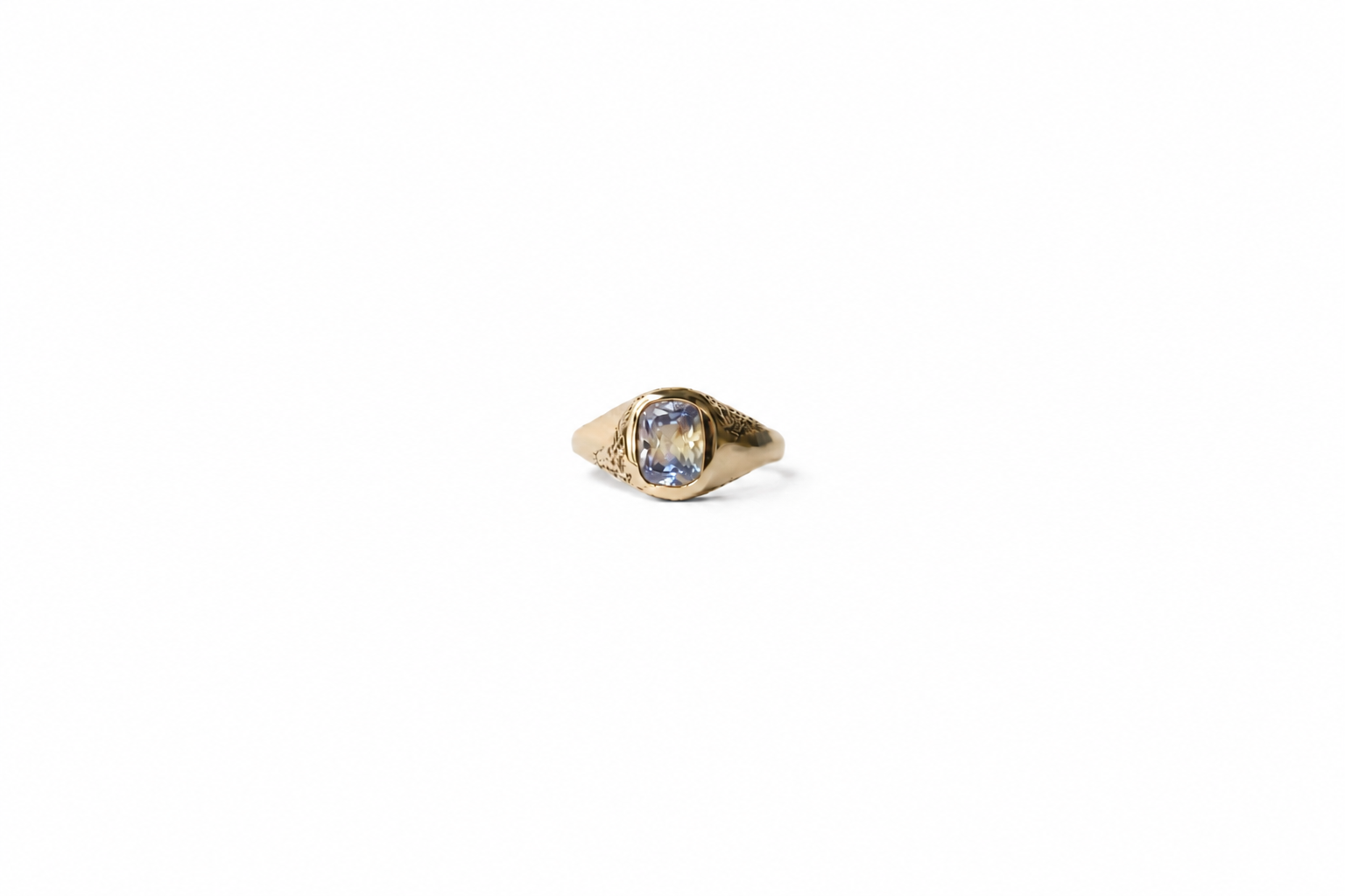 A yellow gold signet ring with a cushion-cut parti sapphire, on a plain white background.