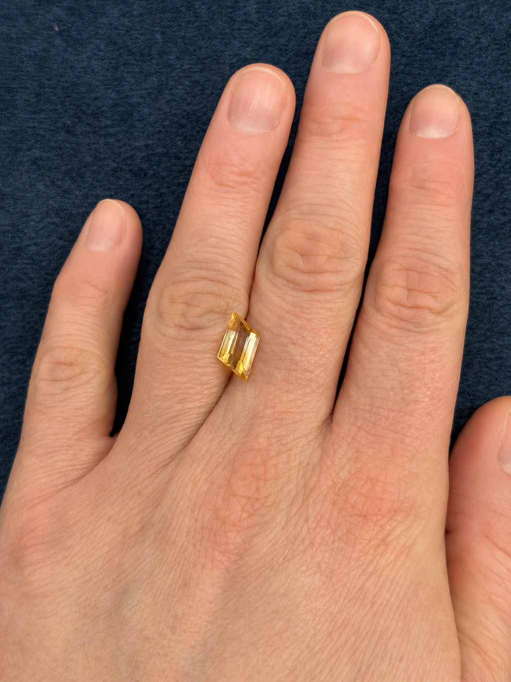 Loose bi-coloured citrine gemstone on a person's finger against a dark blue background