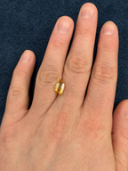 Loose bi-coloured citrine gemstone on a person's finger against a dark blue background