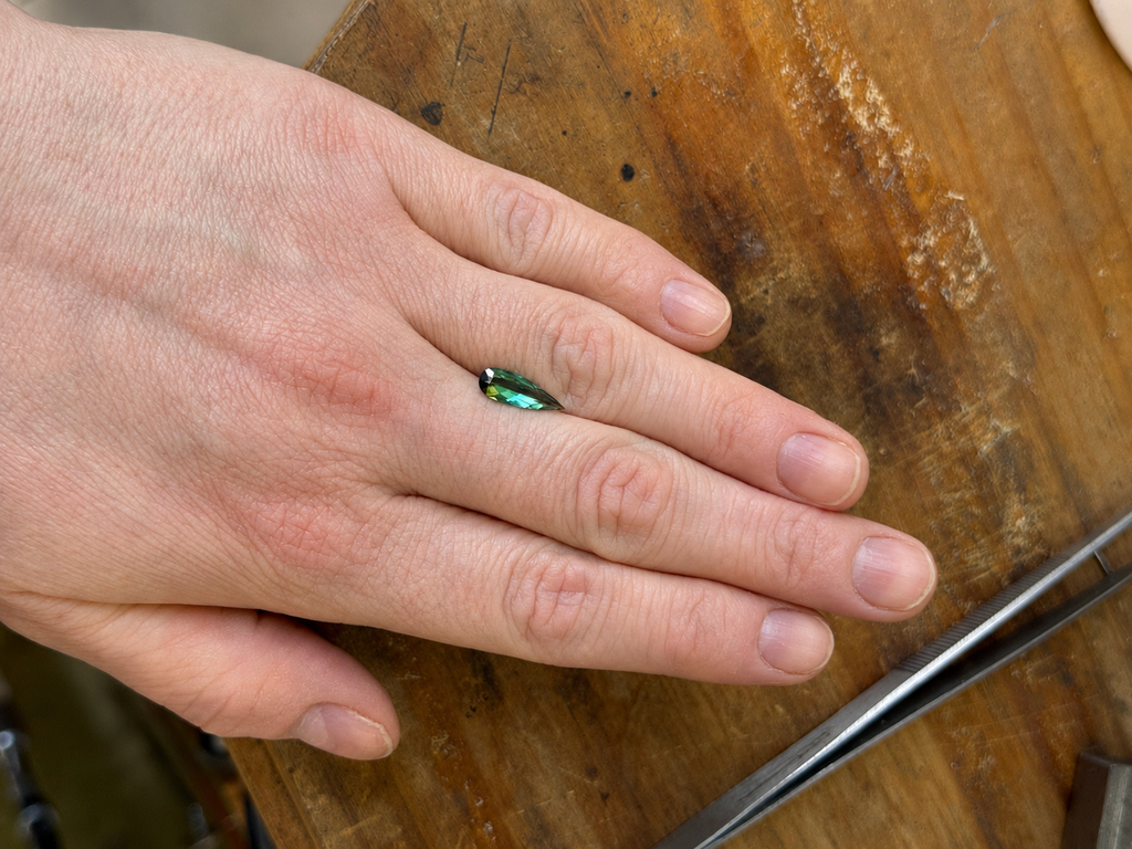 Loose elongated pear shape dark green tourmaline on a persons hand for scale