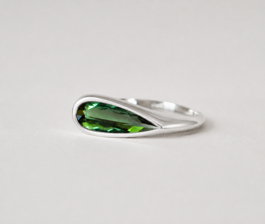3d render of an elongated pear shape dark green tourmaline set in a sterling silver bezel set ring