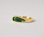 3d render of an elongated pear shape dark green tourmaline set in a yellow gold bezel set ring