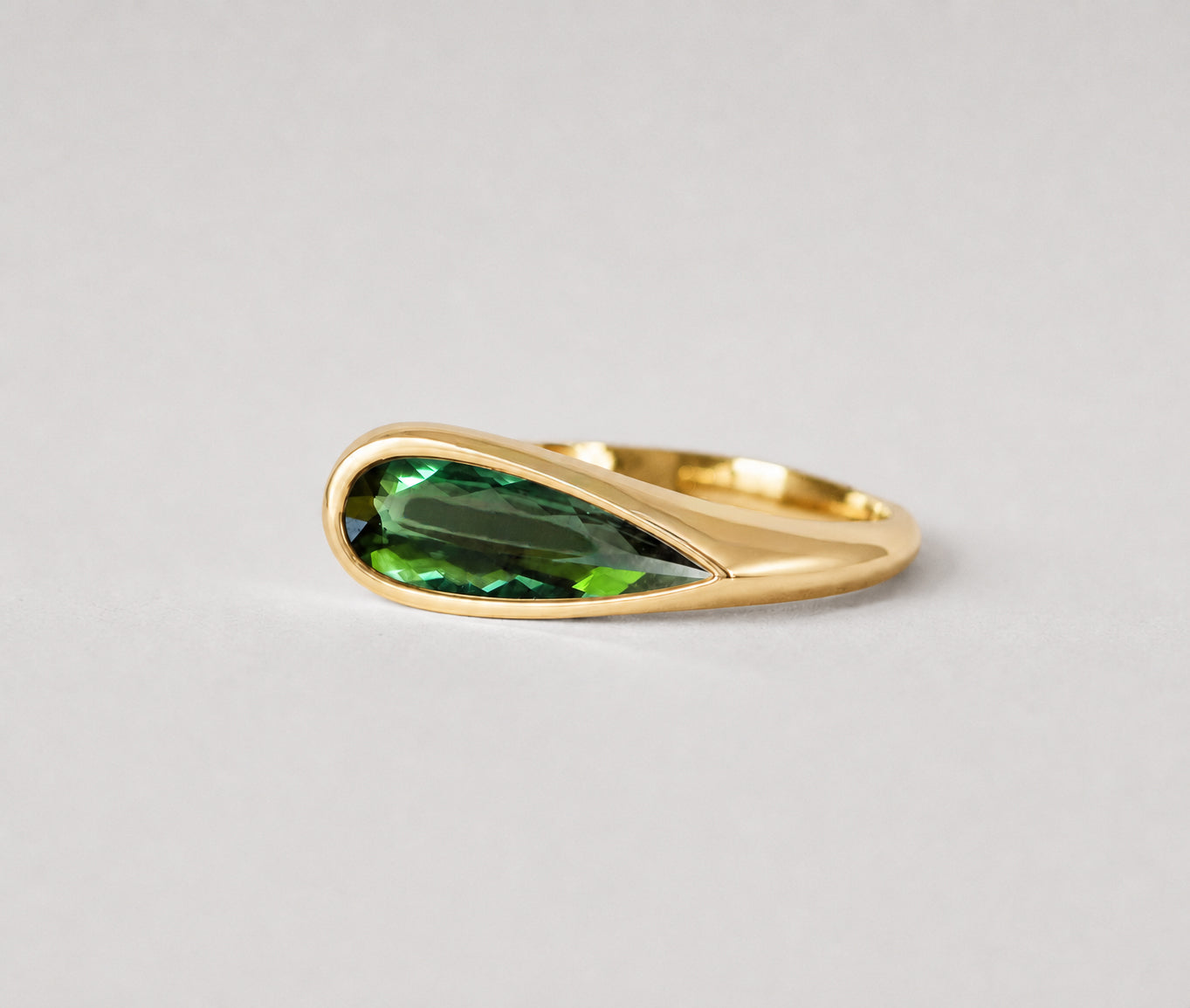 3d render of an elongated pear shape dark green tourmaline set in a yellow gold bezel set ring
