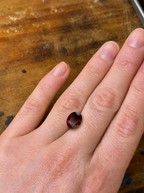 A loose oval deep red almandine garnet on a persons hand for scale
