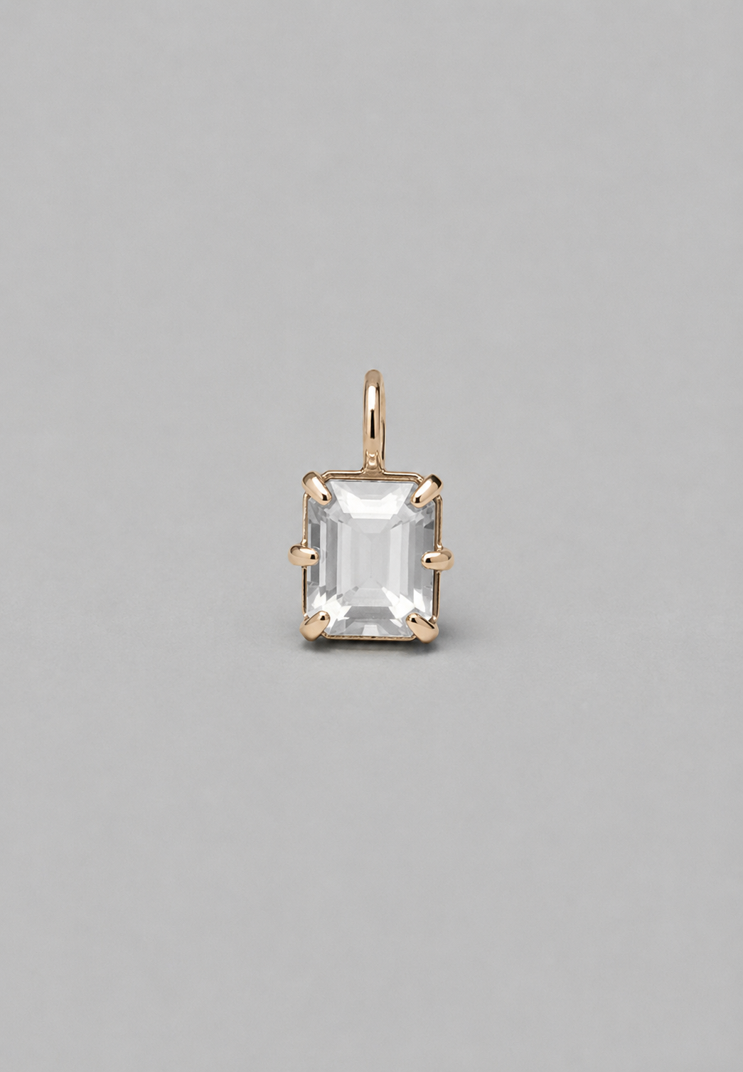 3D render of emerald-cut milky white sapphire pendant in a gold  in a multi claw setting on a solid grey background.