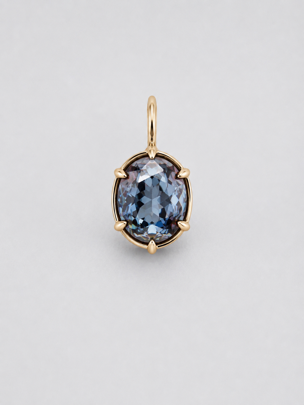 A 3D render of an oval-cut colour change sapphire pendant in a gold multi claw setting with a matching gold bail, shown on a neutral light grey background.