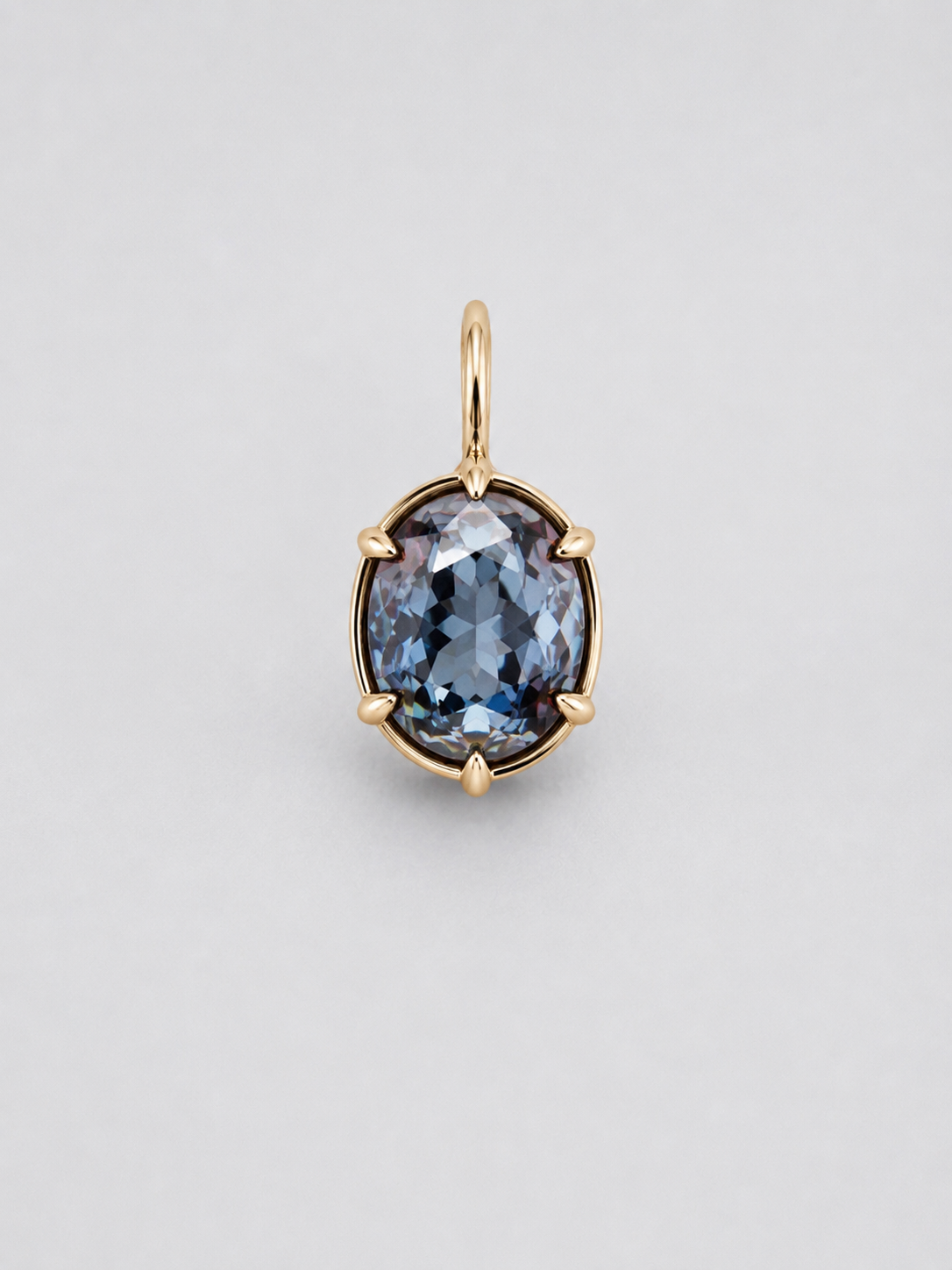 A 3D render of an oval-cut colour change sapphire pendant in a gold multi claw setting with a matching gold bail, shown on a neutral light grey background.