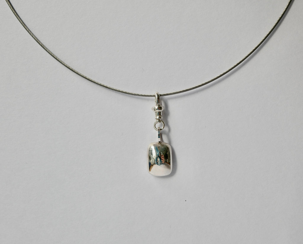 A silver necklace with a thin cord and a small polished silver pendant, photographed against a plain light grey background.