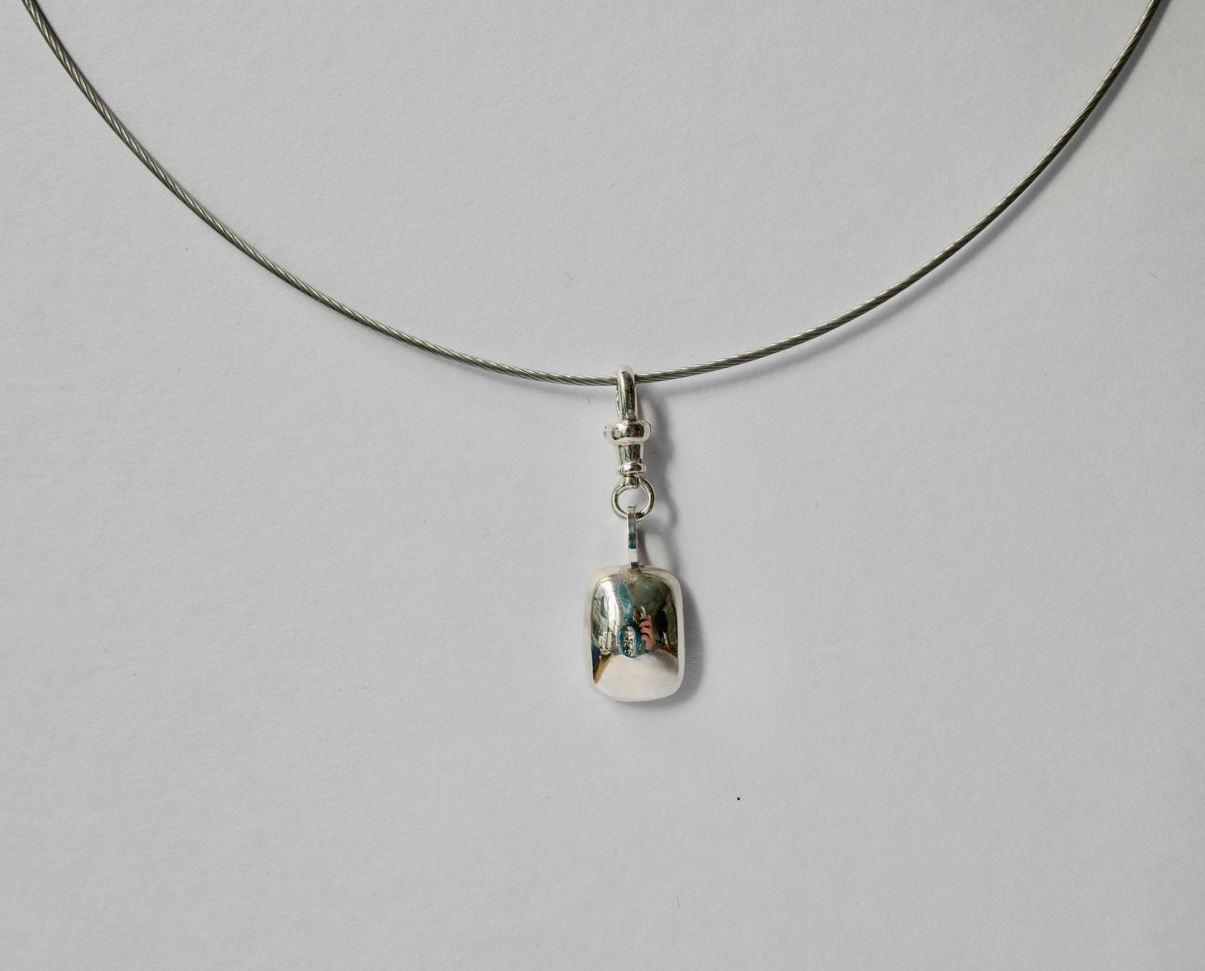 A silver necklace with a thin cord and a small polished silver pendant, photographed against a plain light grey background.