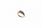 A textured gold ring featuring an openwork band and a central oval blue sapphire, shown on a plain white background.