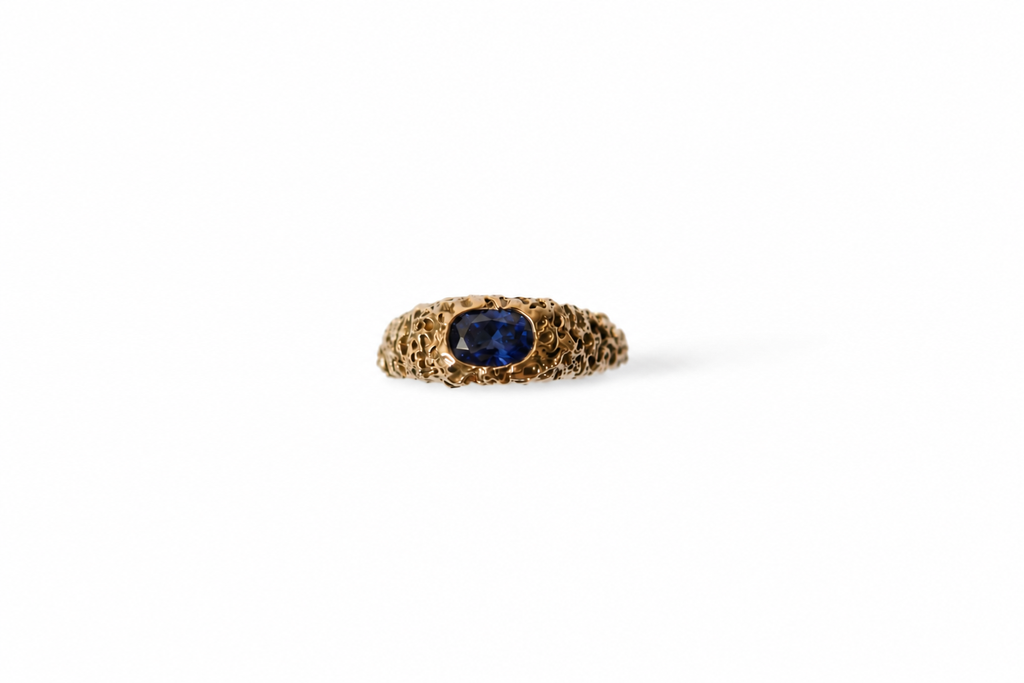 A gold ring with a textured band and a central oval blue sapphire, shown on a plain white background.