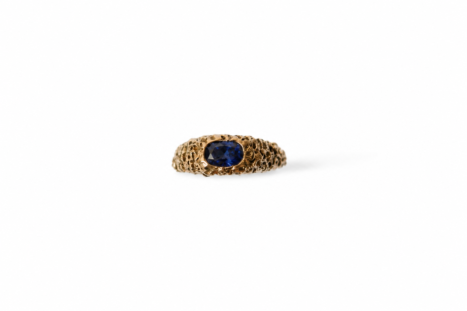 A gold ring with a textured band and a central oval blue sapphire, shown on a plain white background.