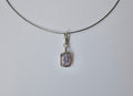 A delicate silver-toned necklace with a small rectangular pendant featuring a lavender-purple amethyst, shown against a plain light grey background.