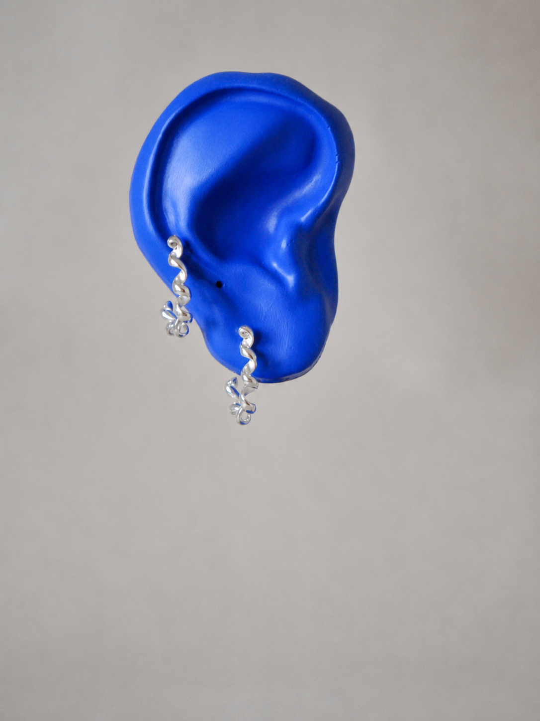 A pair of silver spiral drop earrings, displayed on a bright blue ear against a plain light grey background.