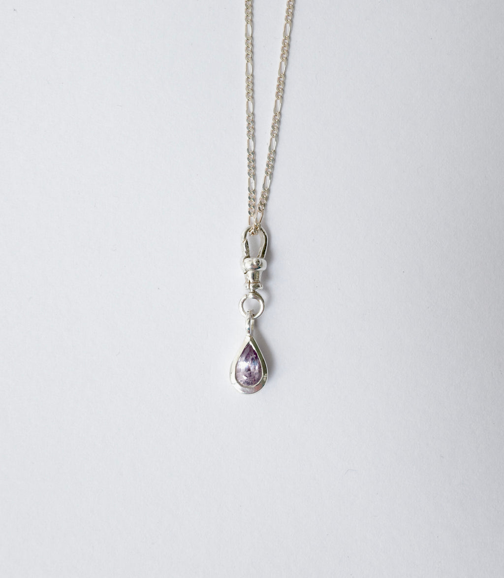 A silver chain necklace with a lobster clasp and a teardrop-shaped purple sapphire pendant, shown against a plain light grey background.