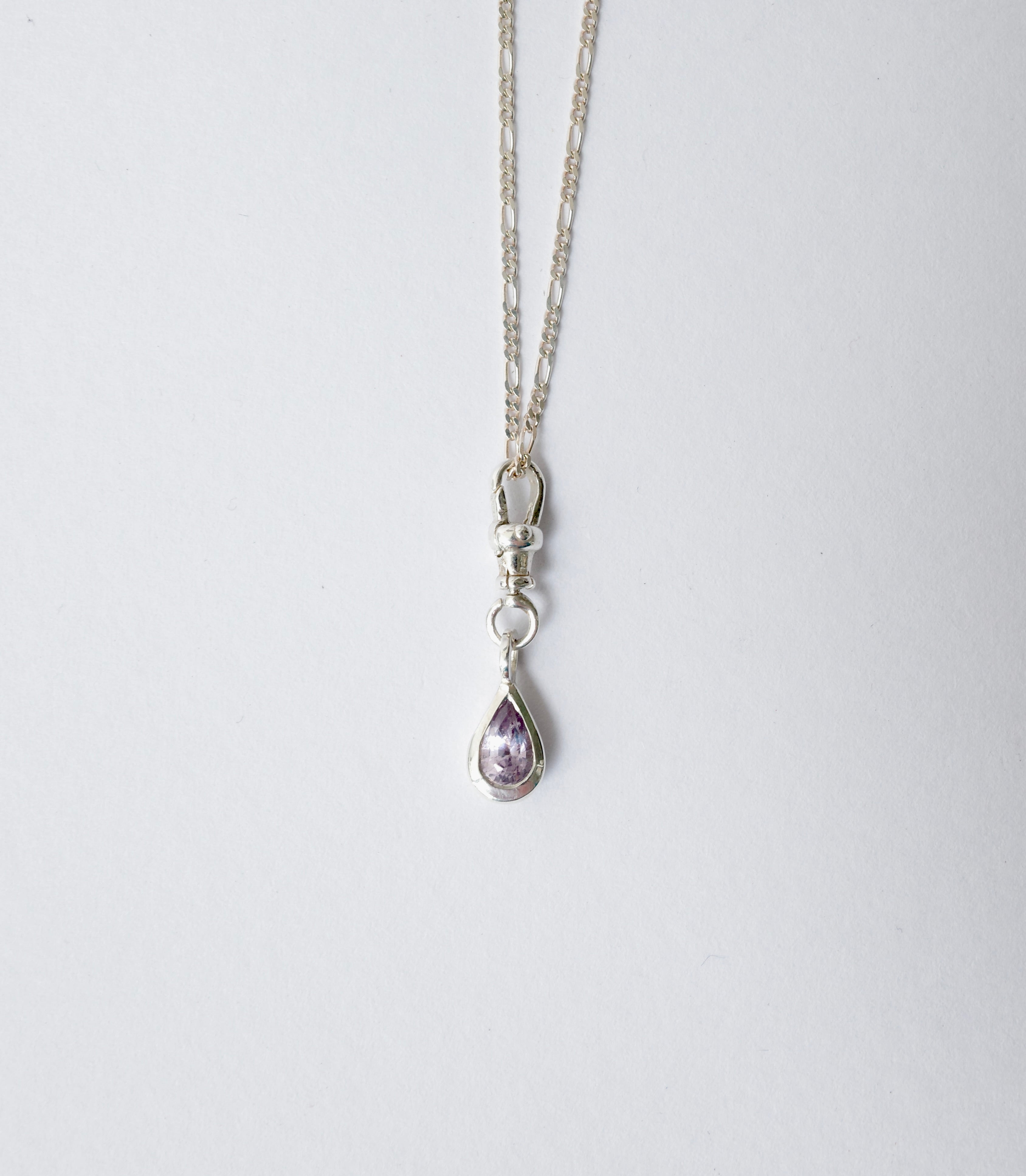 A silver chain necklace with a lobster clasp and a teardrop-shaped purple sapphire pendant, shown against a plain light grey background.