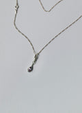 A silver chain necklace with a small teardrop-shaped pendant featuring a light purple sapphire, displayed on a light grey background.