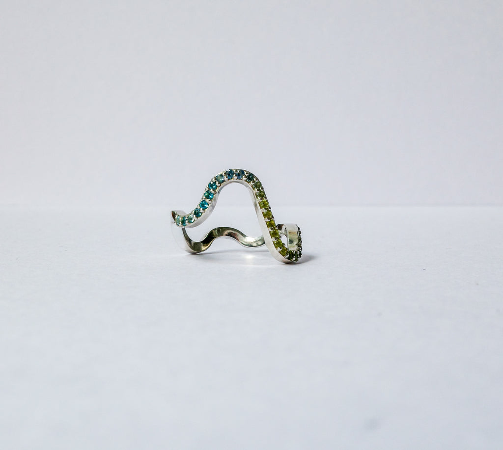 A silver wavy pavé ring adorned with green gemstones, photographed on a plain white background.