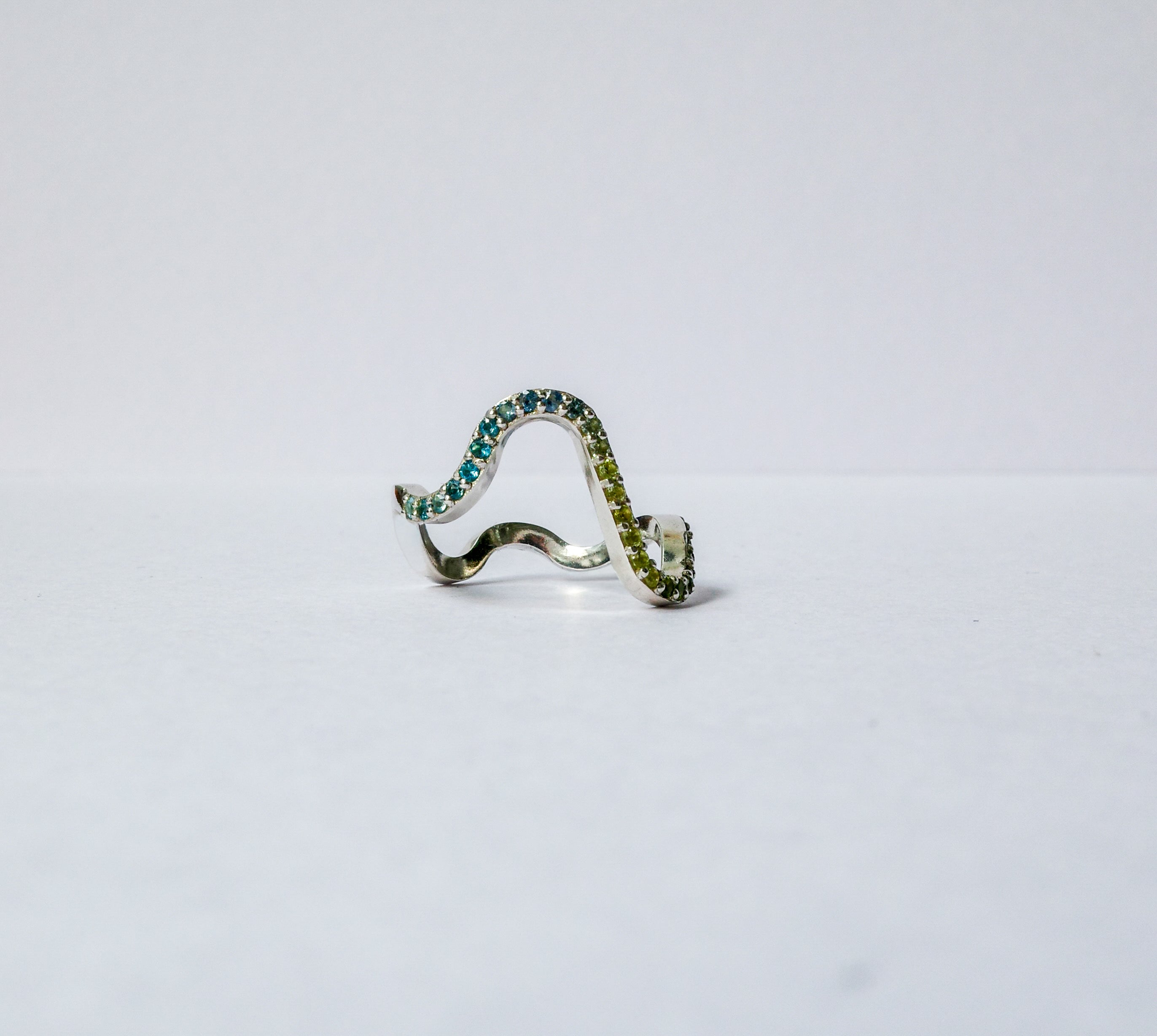 A silver wavy pavé ring adorned with green gemstones, photographed on a plain white background.