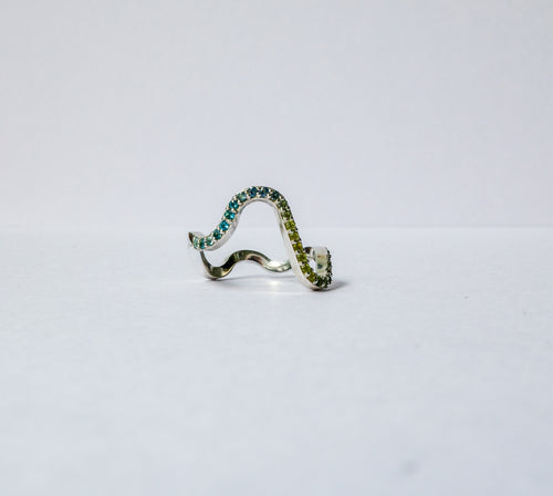 A silver wavy pavé ring adorned with green gemstones, photographed on a plain white background.