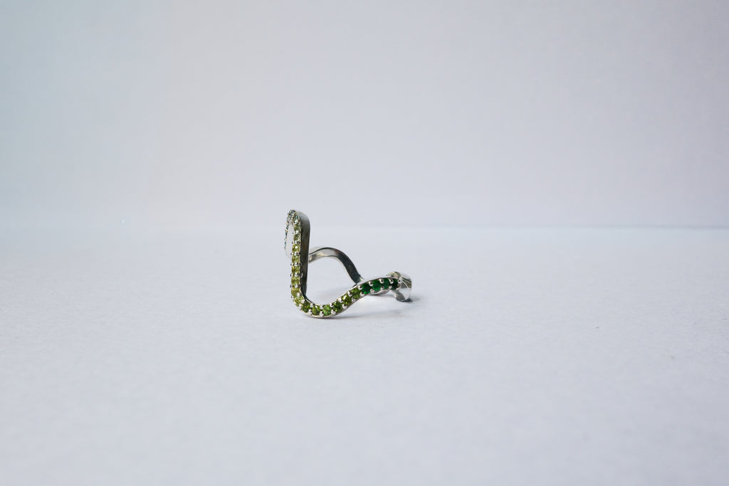 A silver wavy pavé  ring with green gemstone accents, photographed on a plain light gray background.