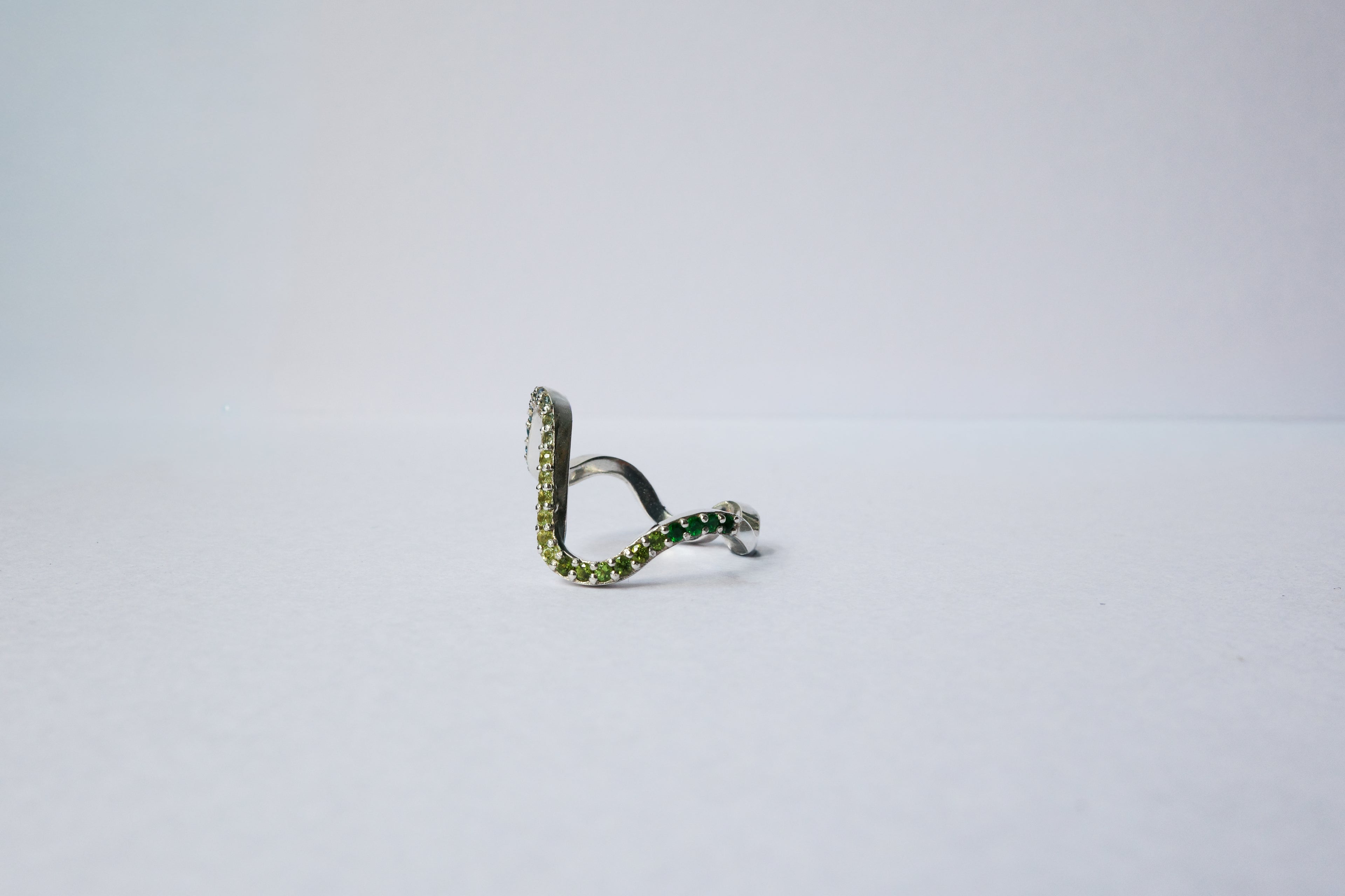 A silver wavy pavé  ring with green gemstone accents, photographed on a plain light gray background.