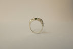 A silver textured ring with a small green sapphire, photographed against a plain light beige background.