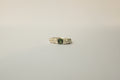 A textured silver ring featuring a central round green sapphire flanked, set against a plain light grey background.