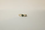 A textured silver ring featuring a central round green sapphire flanked, set against a plain light grey background.