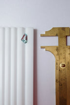 A loose freeform light blue aquamarine on a gemstone sorting tray next to brass callipers for size and scale context