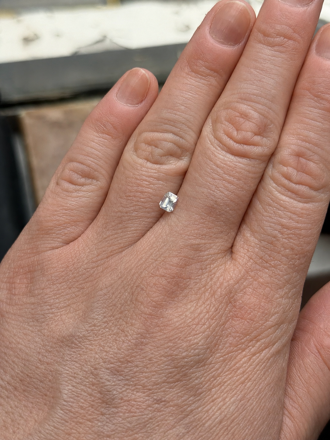 Milky white loose Ceylon sapphire on hand, emerald cut