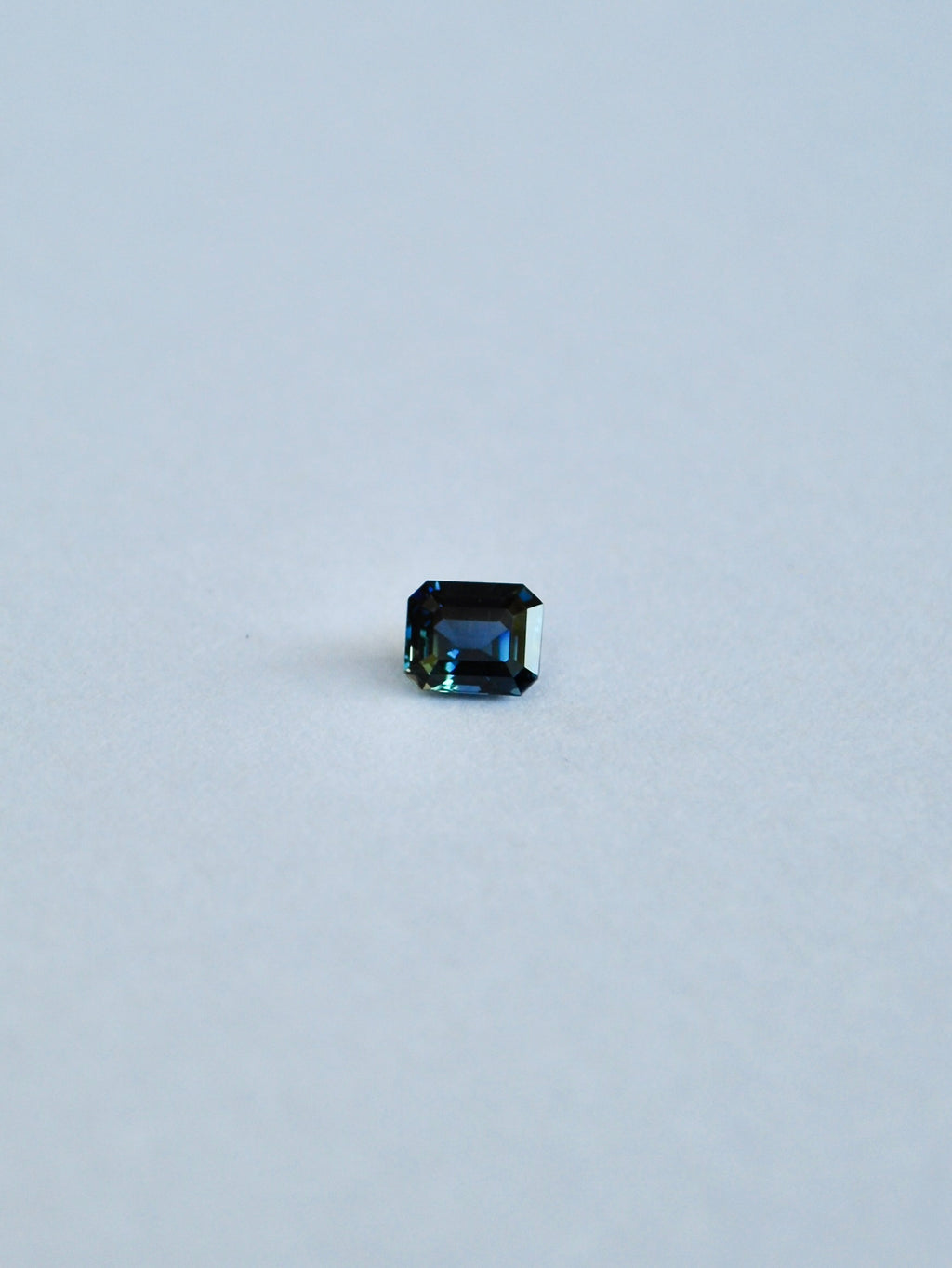 A loose emerald cut blue/green parti sapphire on a white background