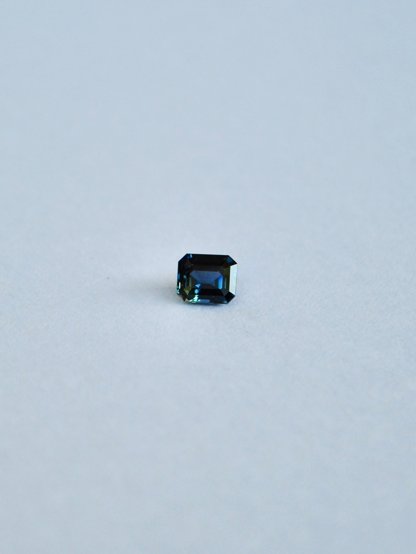 A loose emerald cut blue/green parti sapphire on a white background