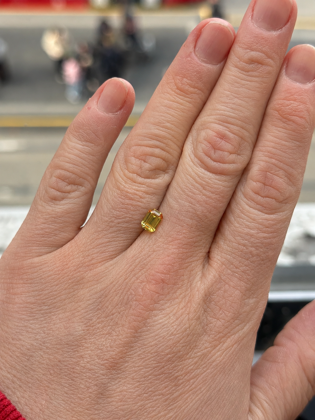 Loose yellow emerald cut Australian sapphire on a persons hand for scale