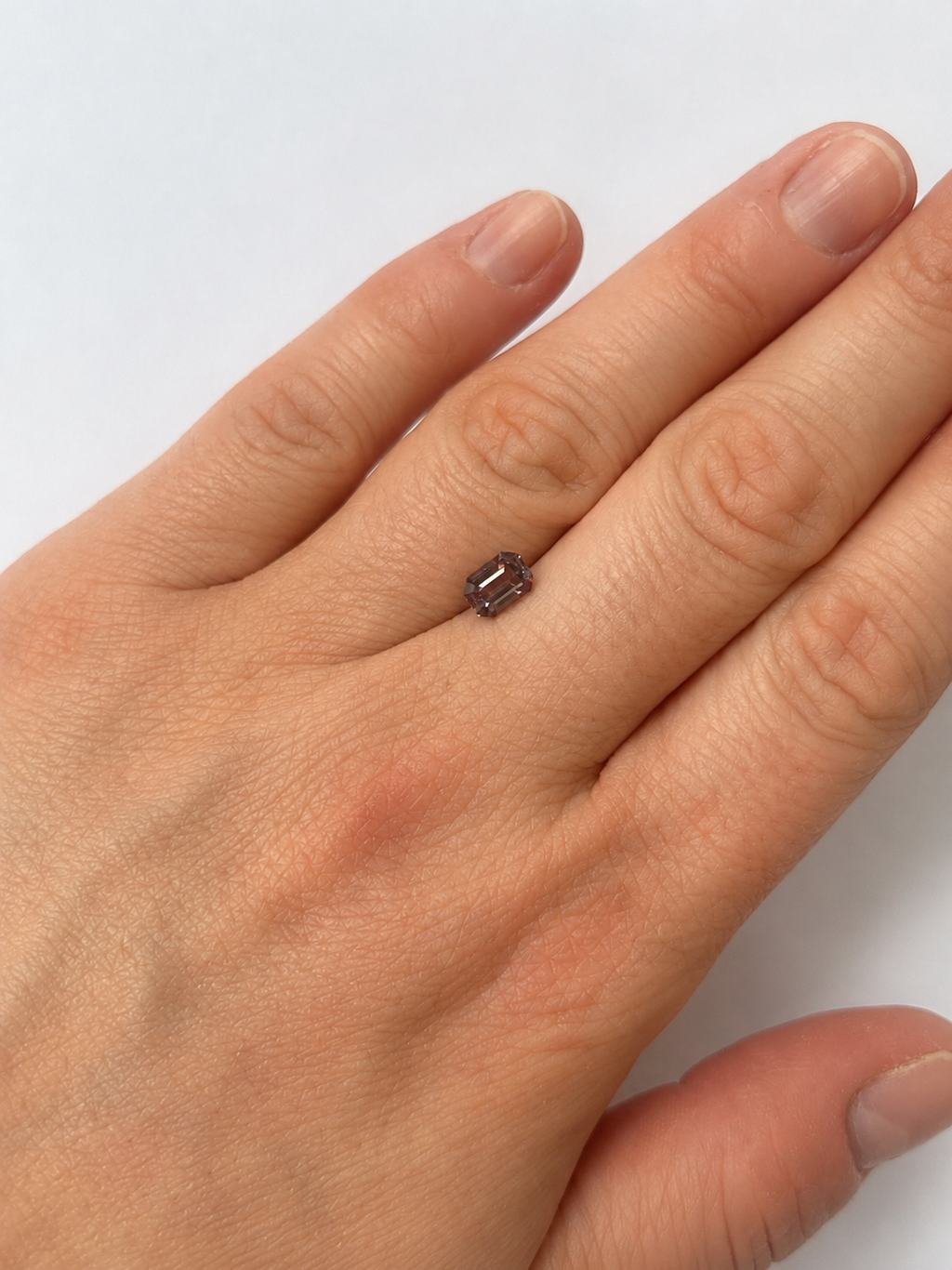 A loose purple emerald cut Spinel on a persons hand for scale