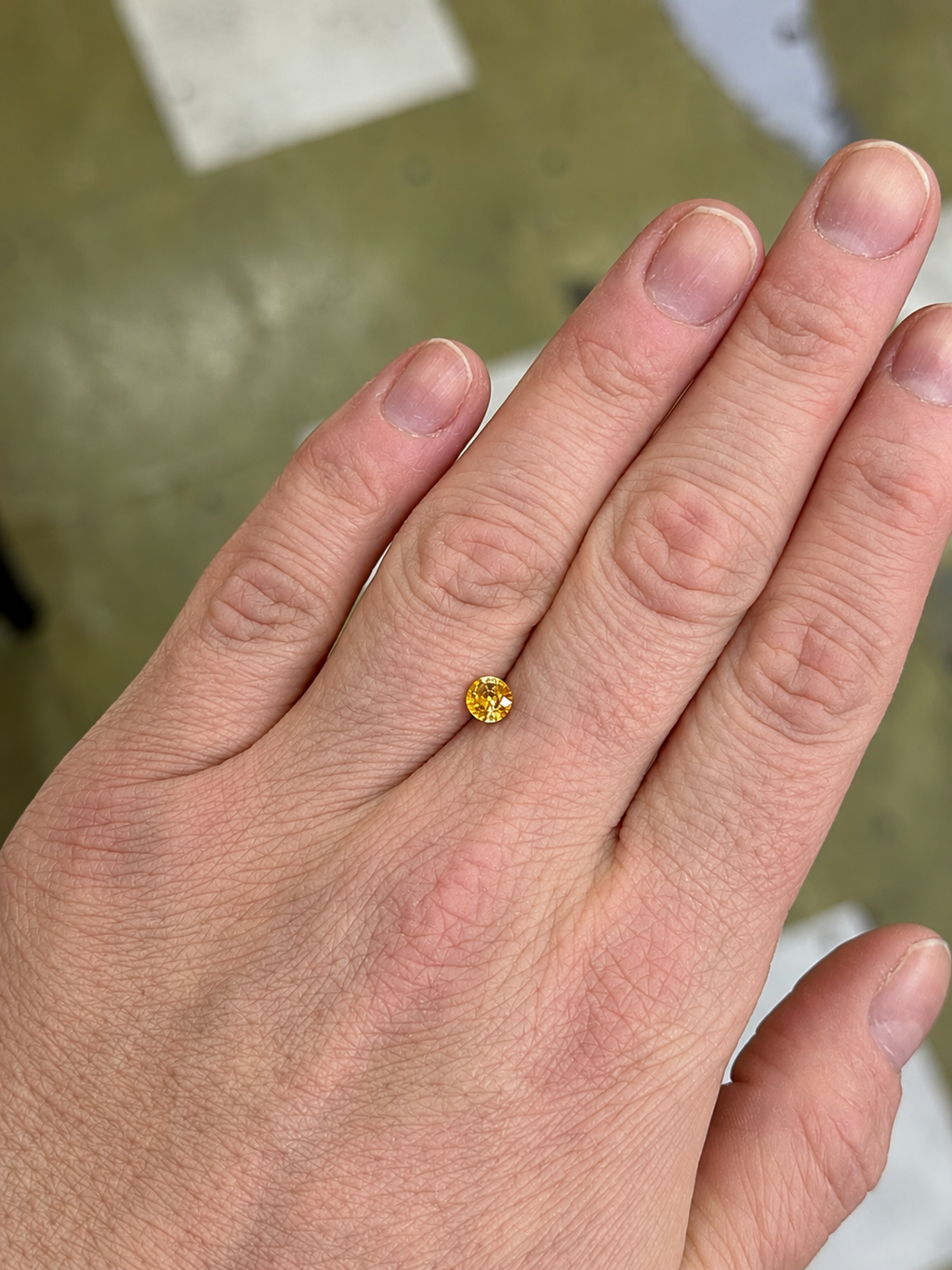 Bi-colour yellow loose round sapphire on a persons hand for scale