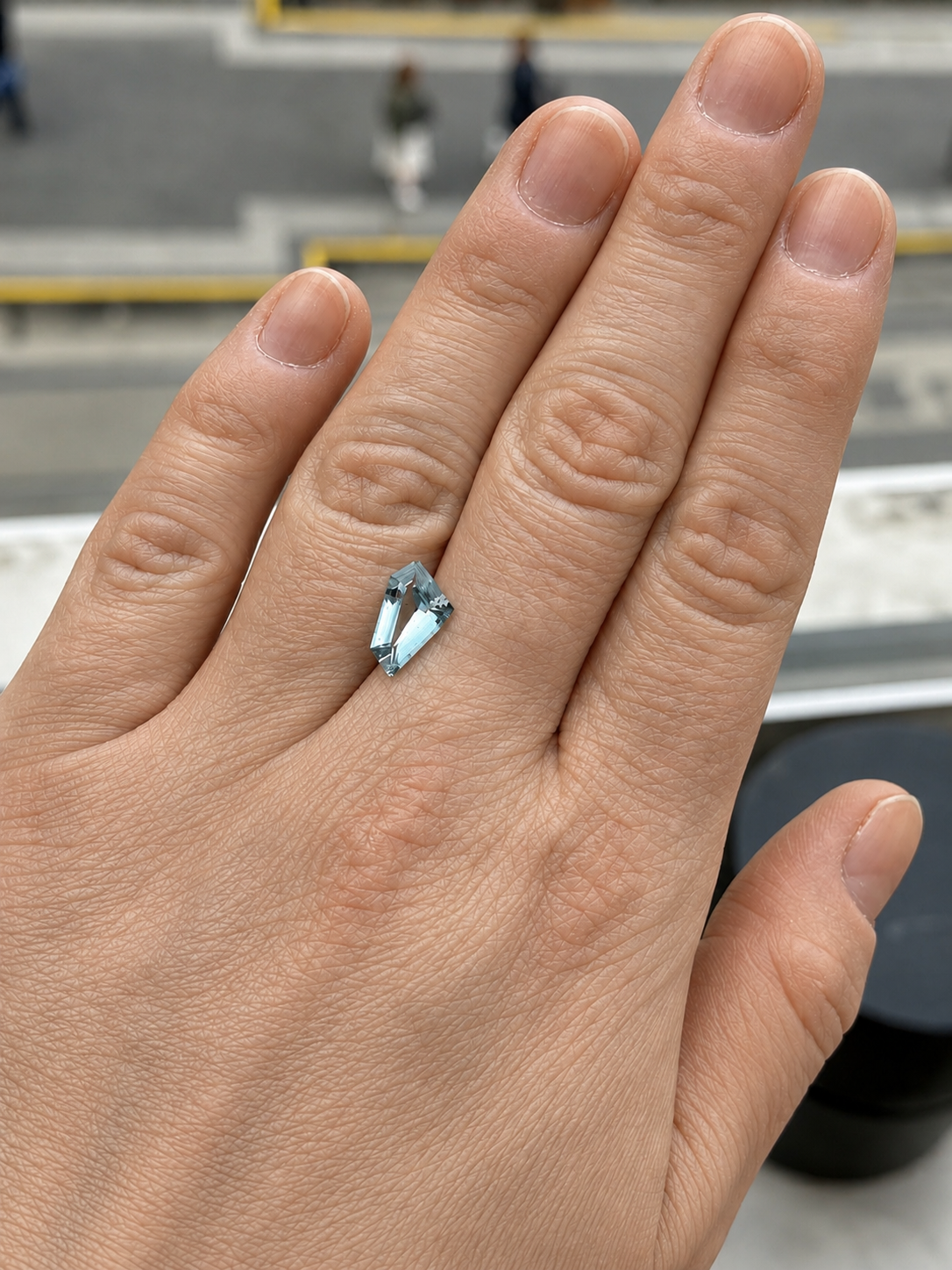 A loose freeform light blue aquamarine on a persons hand for scale