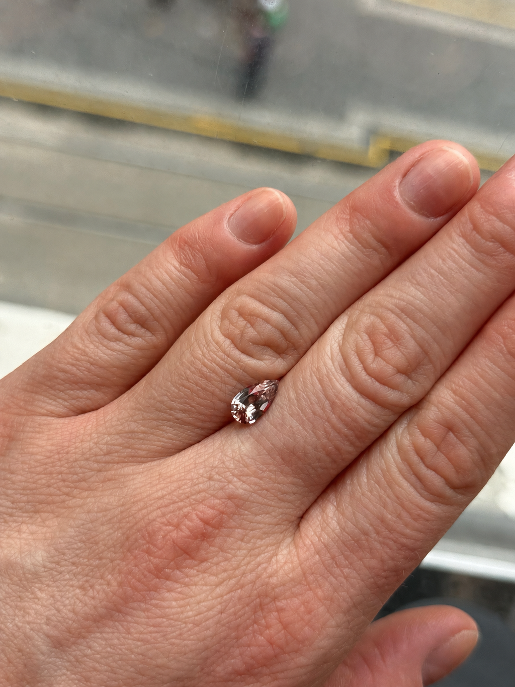 A close-up of a hand a loose champagne pear shaped zircon