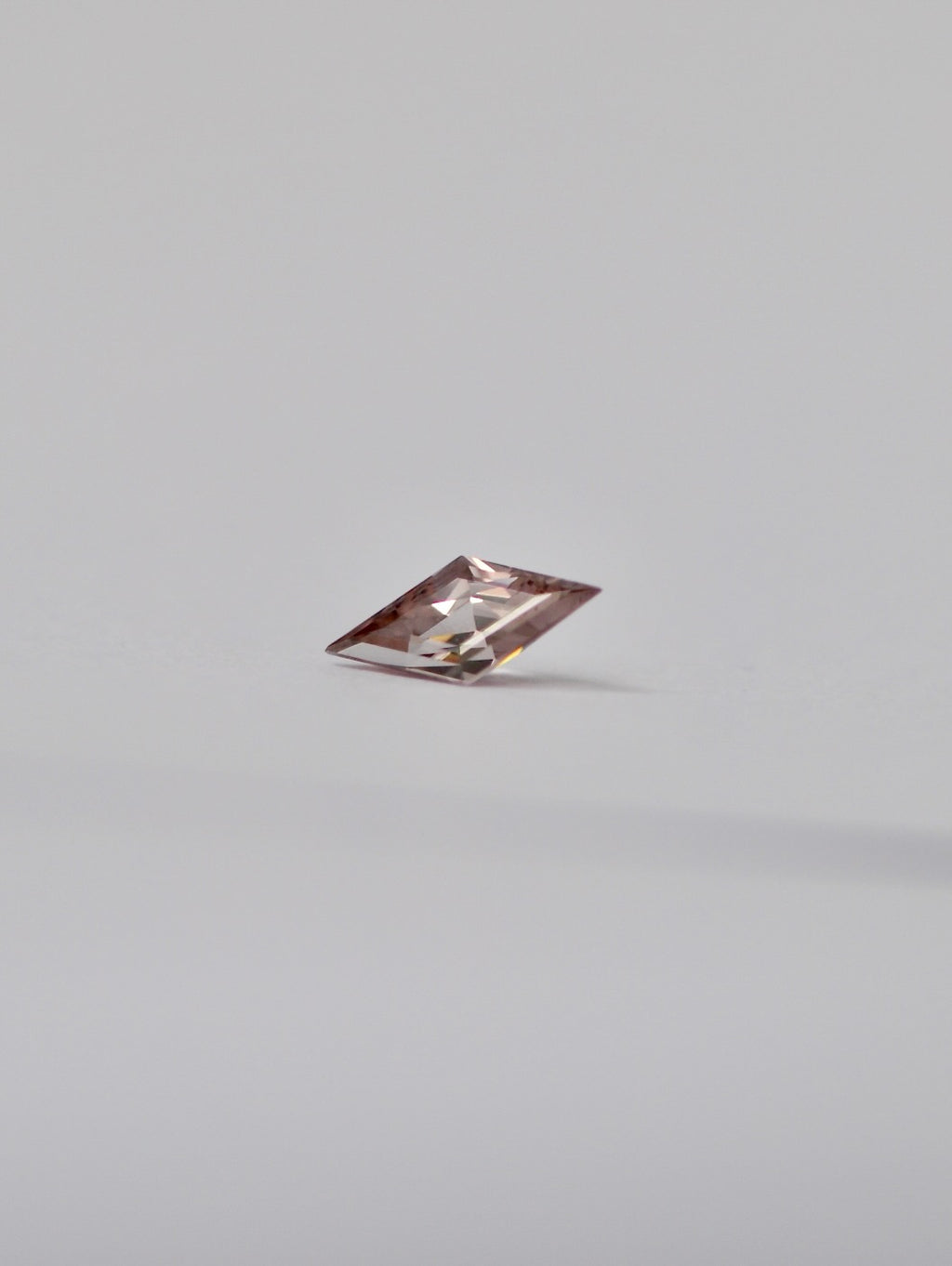 A single loose lozenge dusty pink zircon with a light pinkish-tinted clarity, photographed on a seamless light grey background.