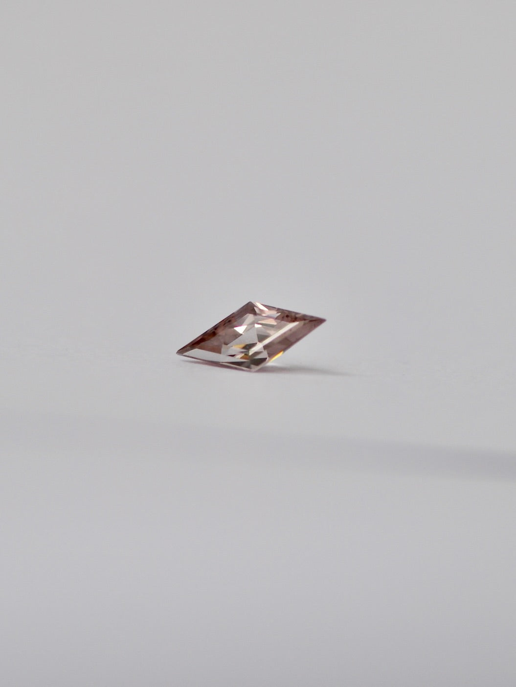 A single loose lozenge dusty pink zircon with a light pinkish-tinted clarity, photographed on a seamless light grey background.