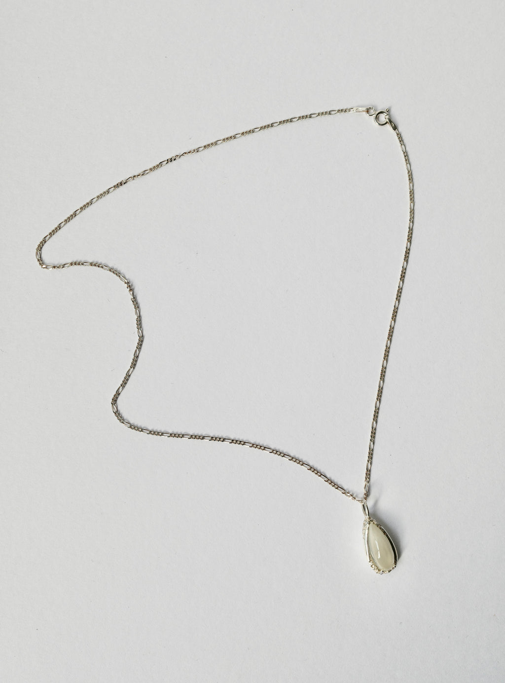 A delicate silver chain necklace with a small, teardrop-shaped milky white moonstone pendant, displayed on a plain light grey background.